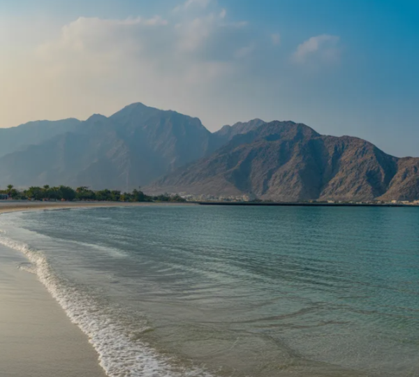 Stunning turquoise waters and sandy shoreline at Khor Fakkan Beach with Hajar Mountains backdrop on UAE east coast