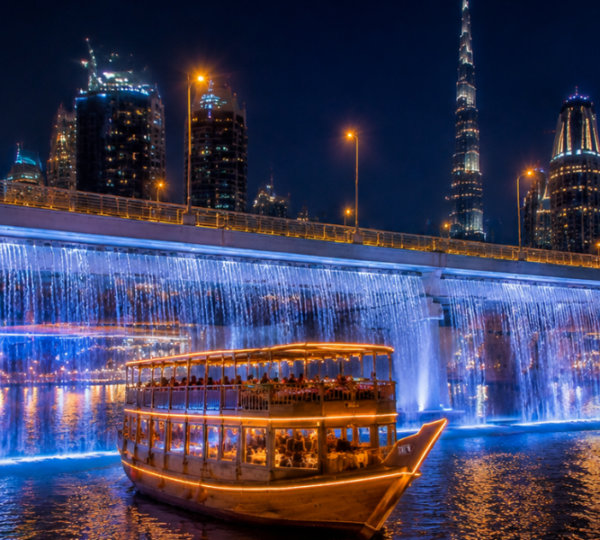 Traditional dhow passing under Sheikh Zayed Road waterfall bridge on Dubai Water Canal with Business Bay skyline at night