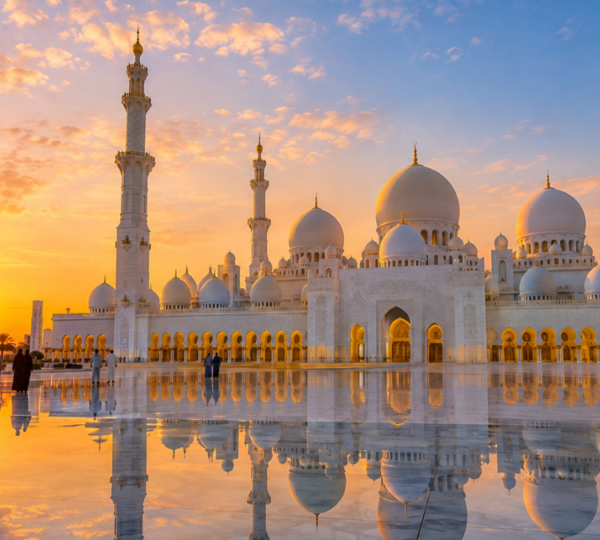 Sheikh Zayed Grand Mosque Abu Dhabi – Sunrise Tour | Zutours Sheikh Zayed Grand Mosque in Abu Dhabi at sunrise with white marble domes reflecting in the pools and visitors walking through the courtyard