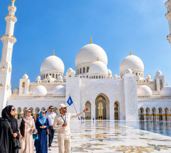Full Day Abu Dhabi Tour – Grand Mosque Courtyard Experience | Zutours Full day Abu Dhabi city tour group exploring Sheikh Zayed Grand Mosque courtyard with guide and reflective pools under blue sky